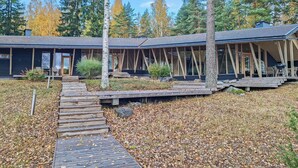Un chalet moderne doté d’un espace extérieur couvert avec des sièges, d’une terrasse en bois et surplombant une forêt naturelle.