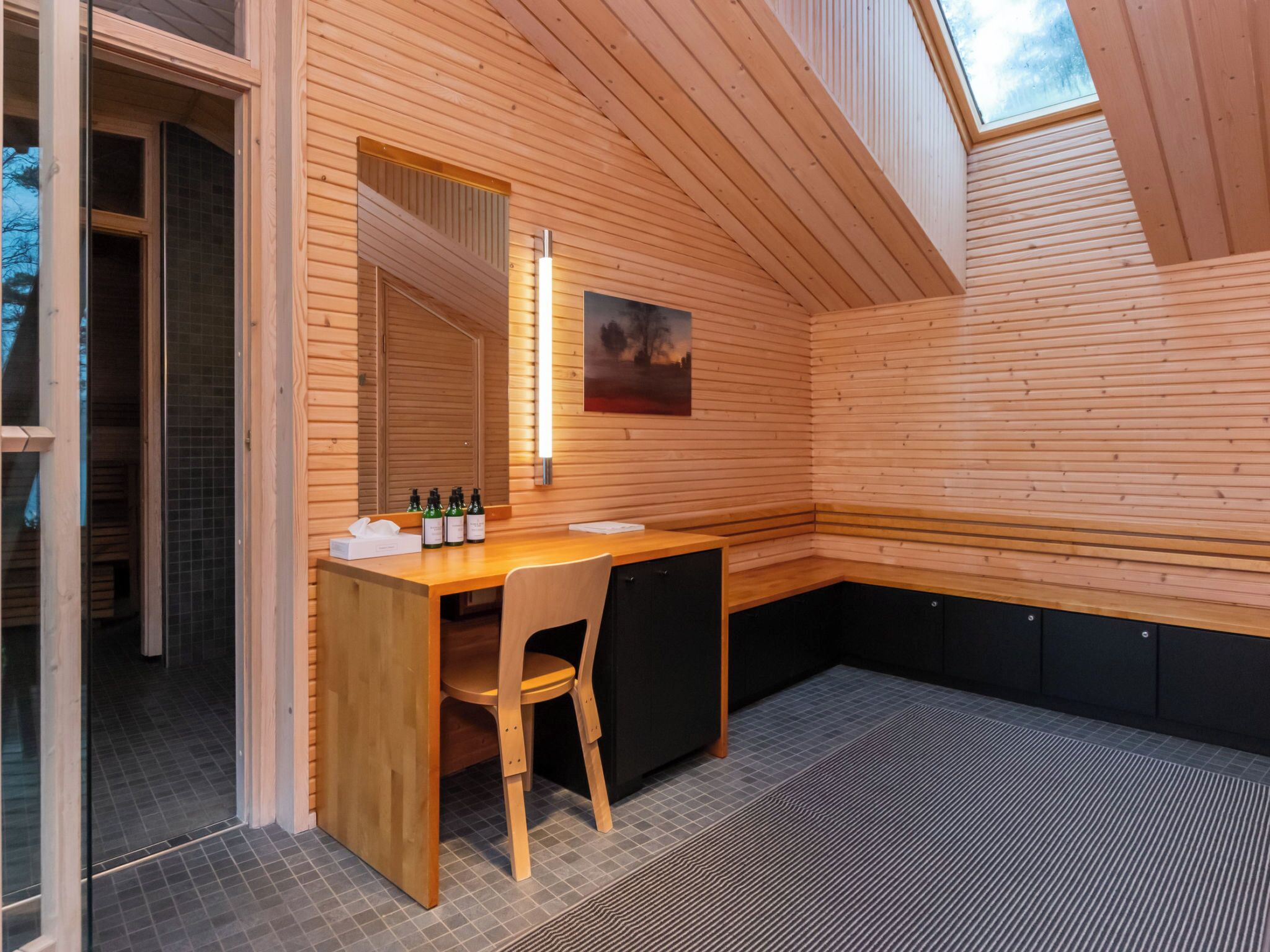 A wooden interior with a desk, chair, and a painting on the wall.