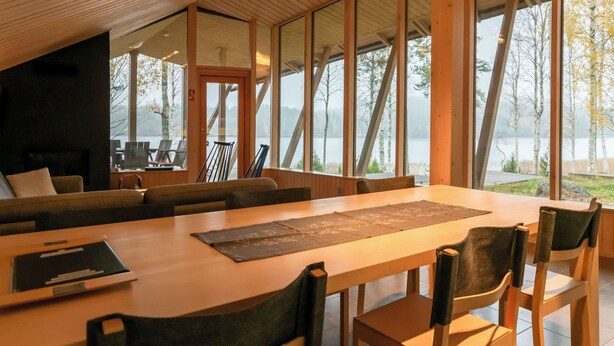 Un intérieur moderne avec un plafond en bois, de grandes fenêtres, un coin repas et une vue sur un lac.