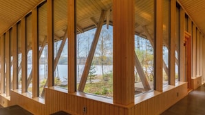 Interior de madera con ventanas amplias, piso de baldosas y vista a un lago.