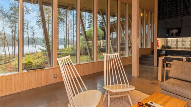 Un interior moderno con ventanas amplias, vigas de madera, una zona de estar y una cocina.
