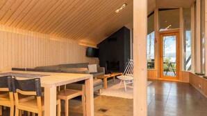 Un interior moderno con techo de madera, zona de comedor, sofá, televisor y vistas a través de un ventanal.