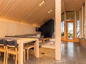 A modern interior with a wooden ceiling, a dining area, a sofa, a TV, and a view through a glass door.