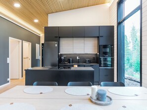 Une cuisine moderne dotée d’un îlot central, d’appareils électroménagers intégrés et d’une grande fenêtre offrant une vue sur l’extérieur.