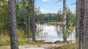 Un cadre paisible au bord d’un lac, avec une jetée en bois et une chaise, le tout entouré d’arbres et sous un ciel dégagé.