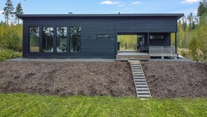Un bâtiment moderne de couleur noire, doté de grandes fenêtres, d’un espace extérieur couvert et d’une terrasse en bois.