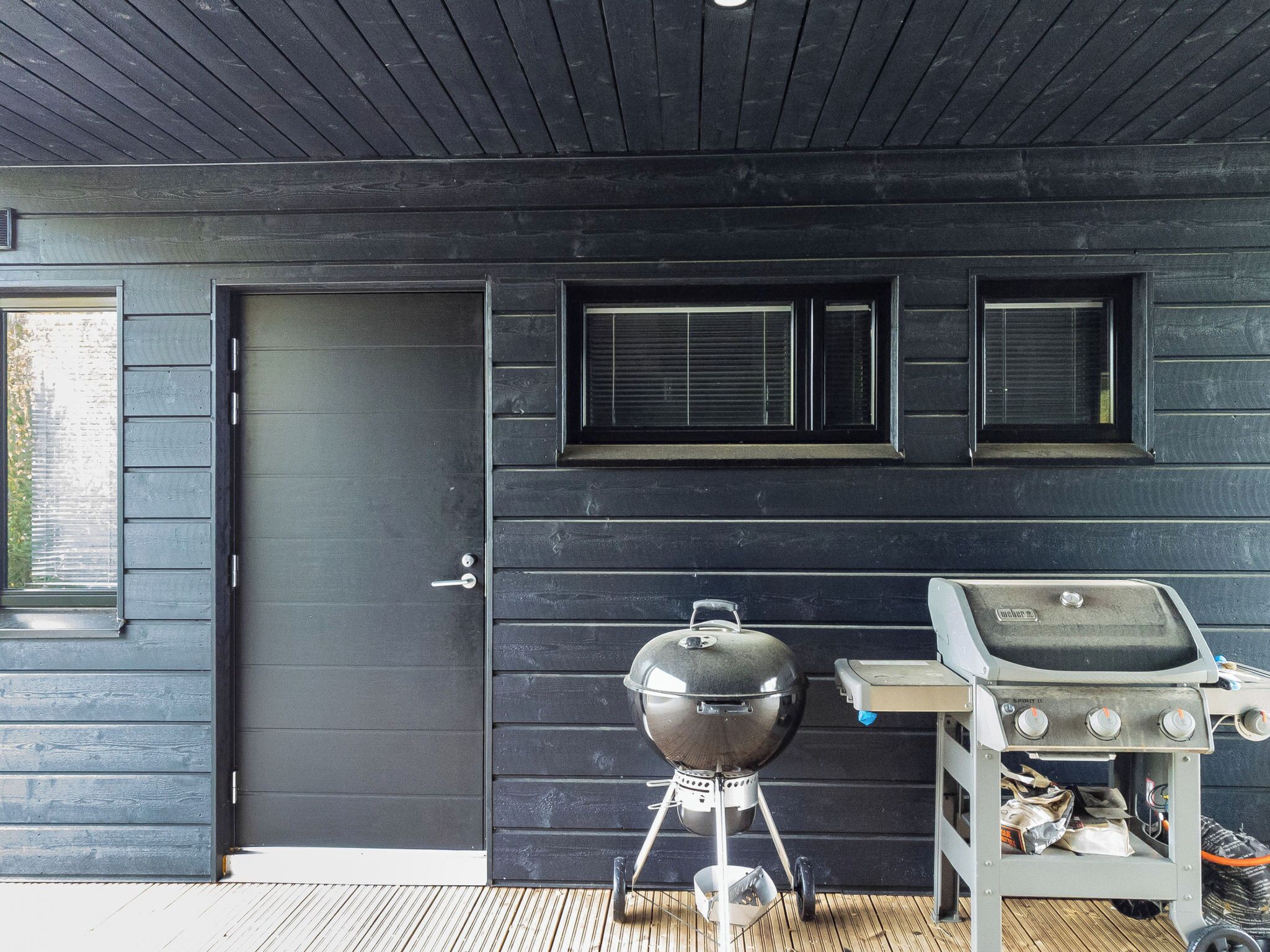 Esterno in legno scuro con una porta, due finestre, un barbecue e una griglia a gas portatile.