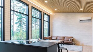 Une cuisine moderne dotée d’un grand îlot central, d’un plafond en bois et de grandes fenêtres offrant une vue sur les arbres.