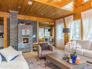 A cozy cabin interior with a fireplace, wooden walls, a dining area, and a living room with a sofa and coffee table.