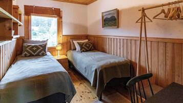 A room with two beds, a wooden ceiling, a hanging light fixture, a painting, and a clothing rack.