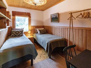 Habitación con dos camas, techo de madera, lámpara colgante, un cuadro y un perchero.