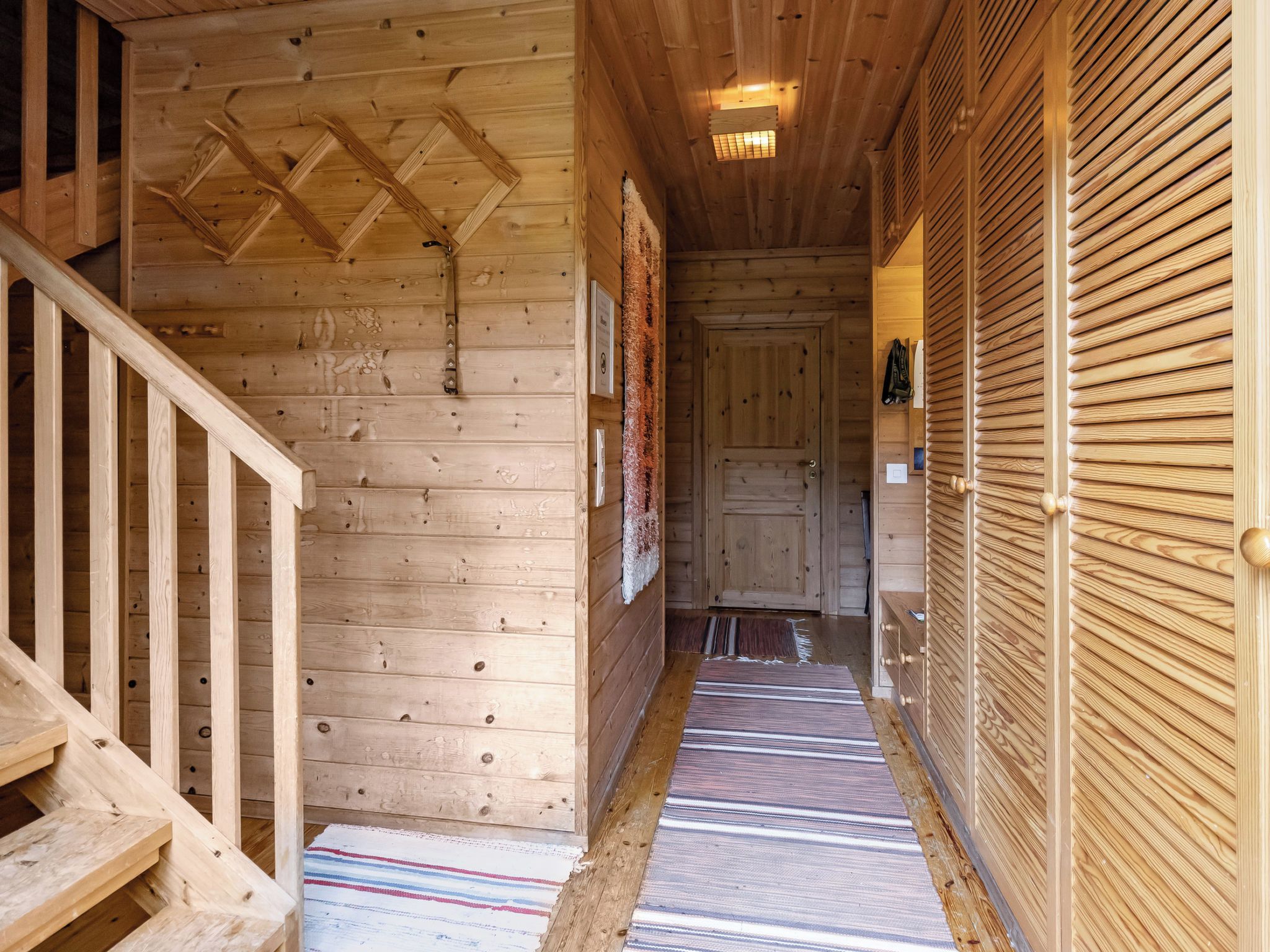 A wooden interior hallway with a staircase, a door, and a patterned rug.