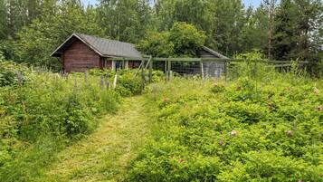 A rural landscape with a wooden barn and a smaller structure, surrounded by dense greenery and a clear sky.