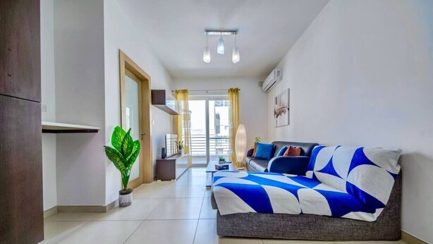Een moderne woonkamer met een bank, een kamerplant en uitzicht naar buiten.