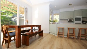 A modern kitchen with wooden bar stools, a dining table with chairs, and a view of greenery outside. - Nine on Wood - Private oasis in the heart of Bright (Bright)