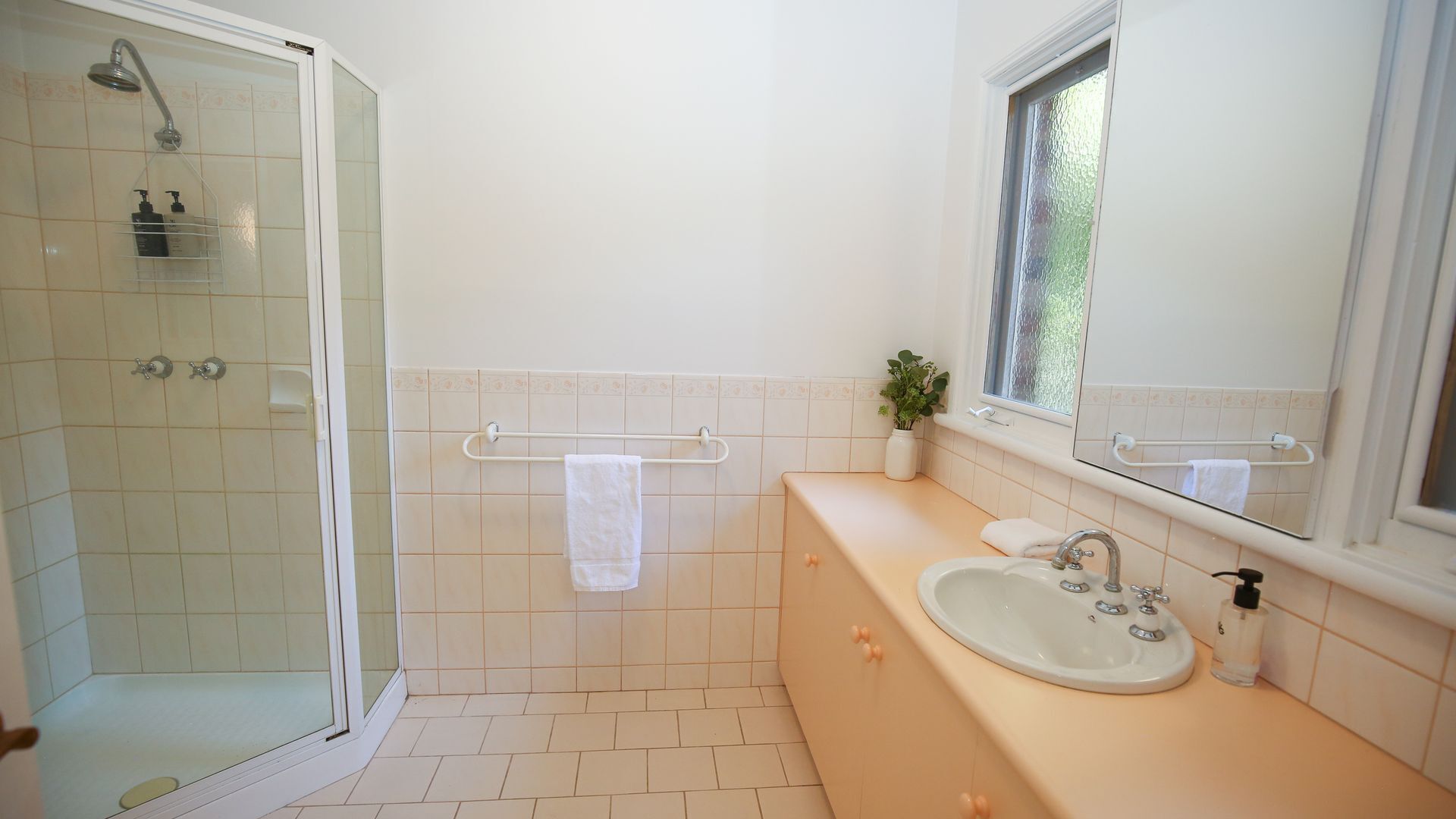 Un baño con ducha, lavamanos, ventana y toallero.
