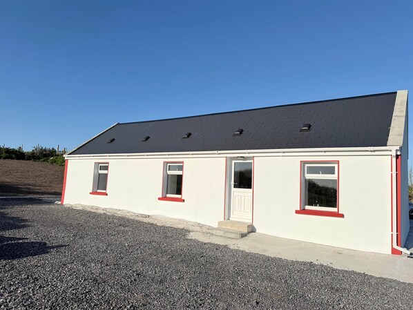 A single-story building with a sloped roof, a gravel driveway, and a clear blue sky.