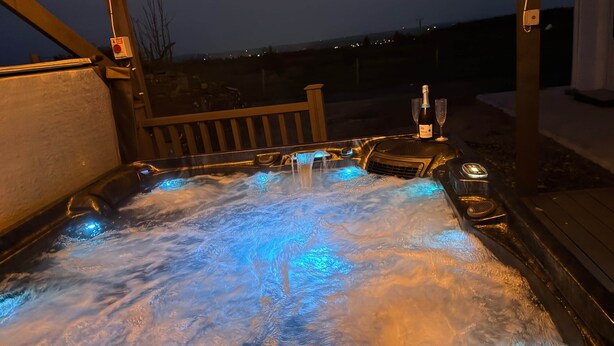 Una vasca idromassaggio con getti, una bottiglia di champagne e due bicchieri su un pontile di legno.