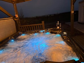 A hot tub with water jets, a bottle of champagne, and two glasses on a wooden deck.