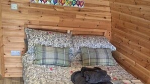 Quarto aconchegante com teto de madeira, cama com roupa de cama estampada e um quadro emoldurado acima da cama.