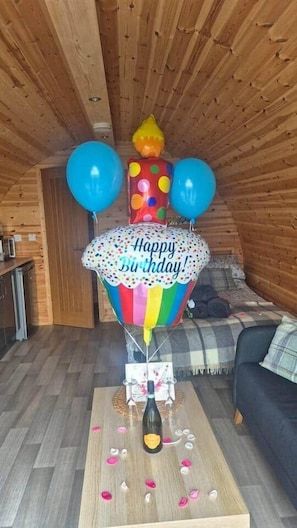 A cozy room with wooden walls, a sofa, a table with a birthday decoration, and a bottle. - Ryeland Pod (Municipal District of Boyle)