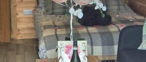A cozy room with a wooden ceiling, a sofa, a small table with a bottle and glasses, and a balloon arrangement with a 'Happy Birthday' sign.