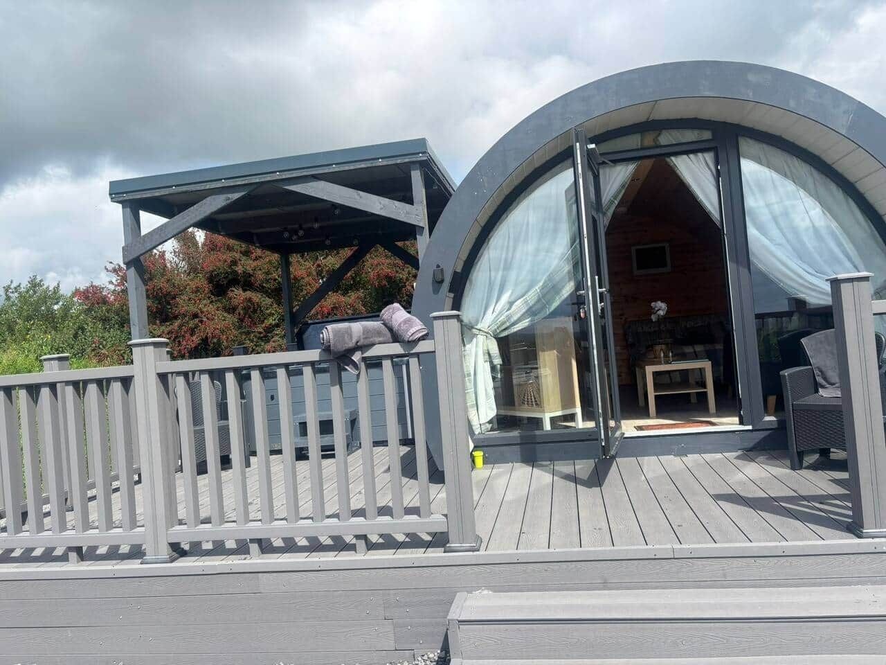 Eine moderne, runde Konstruktion mit überdachtem Außenbereich, einer Holzterrasse und einem kleinen Tisch mit Stühlen.