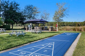 A blue shuffleboard court with picnic tables and an umbrella.