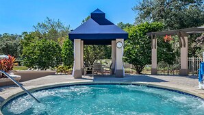 Un jacuzzi con una pérgola, rodeado por una piscina y sillones de descanso.