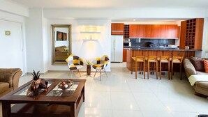 A modern living room with a coffee table, two chairs, a sofa, and a kitchen area with wooden cabinets and a dining table.