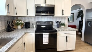 Una cocina con armarios blancos, microondas de acero inoxidable, horno negro, encimeras de granito y salpicadero.