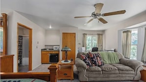 Una habitación con kitchenette, ventilador de techo, sofá y ventana con cortinas.
