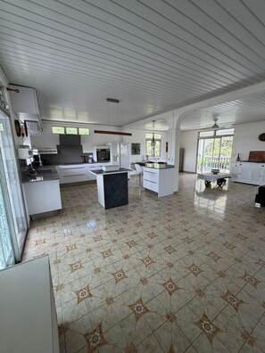 A spacious kitchen with white cabinets, a central island, and a dining area with a table and chairs. - The Attic (Le Robert)