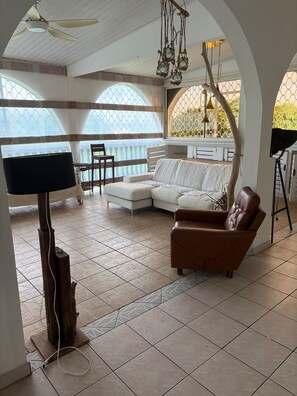 A spacious living area with a white sofa, a brown armchair, a television, and a ceiling fan. - The Attic (Le Robert)