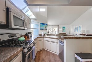 Eine moderne Küche mit integriertem Mikrowellenherd, Herd und Geschirrspüler. Ein Fenster sorgt für natürliches Licht und ein Gemälde ist an der Wand angebracht.