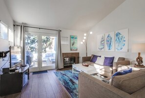 Ein modernes Wohnzimmer mit Kamin, Fernseher und einem großen Fenster mit Vorhängen.