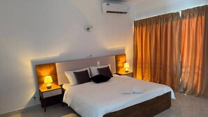 A hotel room with a large bed, two bedside tables with lamps, an air conditioning unit, and curtains. - LA BAIE DE MAERAPH by La Kopell (Assinie)