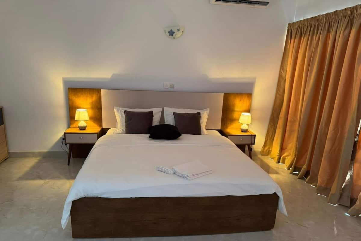 Una habitación de hotel con una cama grande, dos mesitas de noche con lámparas, un cabecero y una cortina.
