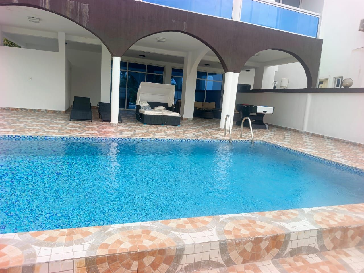 Une piscine intérieure avec un sol carrelé, des chaises longues et un espace de détente abrité.