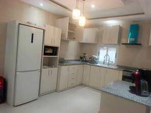 A kitchen with white cabinets, a refrigerator, a microwave, a coffee maker, and a toaster. - LA BAIE DE MAERAPH by La Kopell (Assinie)