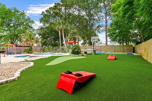 A backyard with artificial grass, a red slide, a pool, and a basketball hoop. - PCB Oasis, Heated Pool, Pickleball, Basketball, Game Room, Mini Golf, Fire Pit (Panama city beach)