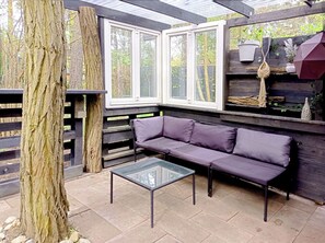 A covered patio with a glass-top table, a purple sofa, and a wooden fence.