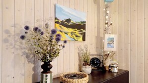 A wooden wall with a painting, a clock, a vase with flowers, and a woven tray on a dark surface.