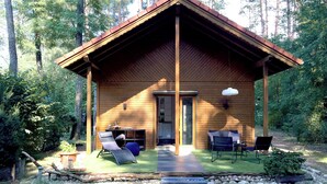 A wooden cabin with a porch, two lounge chairs, a table, and a small garden area.
