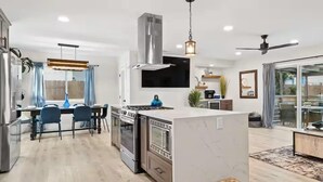 A modern kitchen with a central island, stainless steel appliances, and a dining area with blue chairs.