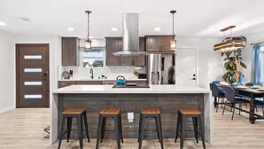 A modern kitchen with a central island, bar stools, stainless steel appliances, and pendant lighting.