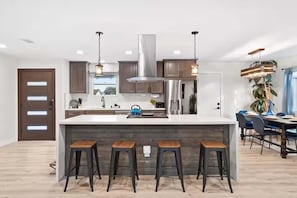 A modern kitchen with a central island, bar stools, stainless steel appliances, and pendant lighting. - Designer Escape with Pool, Firepit, Game Room, BBQ (San Diego)