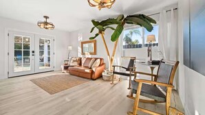 A spacious living room with a large sofa, a wooden rocking chair, a coffee table, and a large plant.