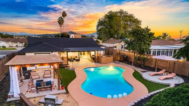 A backyard with a swimming pool, patio furniture, and a covered seating area.