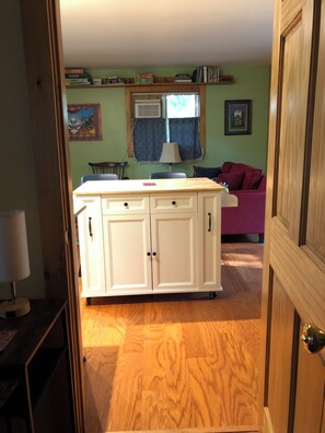 A kitchen with a central island, a dining table, and chairs. There is a purple couch in the background.